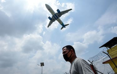 A Jazeera Airways plane approaches to land while a man wearing a facemask as a preventive measure against the spread of the COVID-19 coronavirus walks under at the Tribhuvan International airport in Kathmandu on June 11, 2020. (Photo by PRAKASH MATHEMA / AFP) (Photo by PRAKASH MATHEMA/AFP via Getty Images)