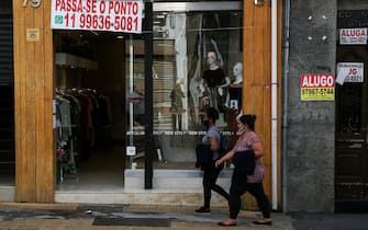 SAO PAULO, BRAZIL - JUNE 29: People wearing face masks walk in front of a shop with a 'For Lease' sign in downtown amidst the coronavirus (COVID-19) pandemic on June 29, 2020 in Sao Paulo, Brazil. Many businesses in the city of Sao Paulo went bankrupt and some commercial spaces are either for sale or for lease during the coronavirus (COVID-19) pandemic. (Photo by Alexandre Schneider/Getty Images)