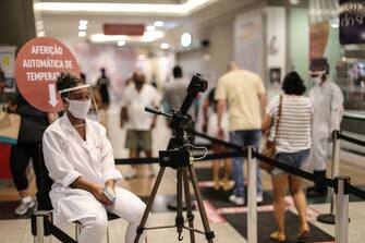 NITEROI, BRAZIL - JULY 01: A worker wearing PPE checks customers temperature at the mall entrance amidst the coronavirus (COVID-19) pandemic on July 1, 2020 in Niteroi, Brazil. The city of Niteroi authorized the reopening of shopping malls and small and medium-sized street business. The establishments will be able to reopen following distance rules such as reduced opening hours, restricting the flow of people and maintaining hygiene standards. (Photo by Luis Alvarenga/Getty Images)