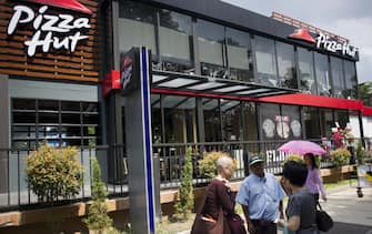 Pedestrians walk outside Pizza Hut's first restaurant in Yangon on October 22, 2015. Pizza Hut is to open its first restaurant in Yangon, the latest major western fast food chain to enter the emerging nation where consumer habits are changing fast. AFP PHOTO / Ye Aung THU / AFP PHOTO / Ye Aung Thu        (Photo credit should read YE AUNG THU/AFP via Getty Images)