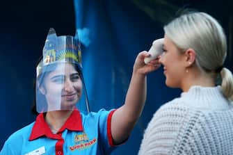 SYDNEY, AUSTRALIA - JULY 03: Luna Park staff member Ida Ghalandari takes the temperature of guests on arrival to the fun park on July 03, 2020 in Sydney, Australia. Sydney's Luna Park has reopened to the public following its temporary closure on Monday 23 March in response to the COVID-19 pandemic. Restrictions on entertainment venues, weddings, community sport and other gatherings have been eased across NSW since 1 July, but strict physical distancing measures remain in place. (Photo by Lisa Maree Williams/Getty Images)