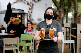 A member of bar staff wearing PPE (personal protective equipment) in the form of a face mask, serves customers with drinks outside the Wetherspoon pub, Goldengrove in Stratford in east London on July 4, 2020, as restrictions are further eased during the novel coronavirus COVID-19 pandemic. - Pubs in England reopen on Saturday for the first time since late March, bringing cheer to drinkers and the industry but fears of public disorder and fresh coronavirus cases. (Photo by Tolga AKMEN / AFP) (Photo by TOLGA AKMEN/AFP via Getty Images)