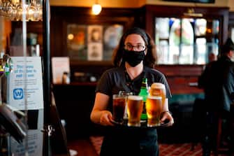 A member of bar staff wearing PPE (personal protective equipment) in the form of a face mask, carries drinks inside the Wetherspoon pub, Goldengrove in Stratford in east London on July 4, 2020, as restrictions are further eased during the novel coronavirus COVID-19 pandemic. - Pubs in England reopen on Saturday for the first time since late March, bringing cheer to drinkers and the industry but fears of public disorder and fresh coronavirus cases. (Photo by Tolga Akmen / AFP) (Photo by TOLGA AKMEN/AFP via Getty Images)