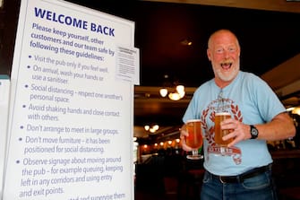 A customer reacts as he walks with two pints of beer past an information board giving advice on new anti-covid measures inside the Wetherspoon pub, Goldengrove in Stratford in east London on July 4, 2020, as restrictions are further eased during the novel coronavirus COVID-19 pandemic. - Pubs in England reopen on Saturday for the first time since late March, bringing cheer to drinkers and the industry but fears of public disorder and fresh coronavirus cases. (Photo by Tolga AKMEN / AFP) (Photo by TOLGA AKMEN/AFP via Getty Images)
