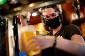 A member of bar staff wearing PPE (personal protective equipment) in the form of a face mask, pours drinks inside the Wetherspoon pub, Goldengrove in Stratford in east London on July 4, 2020, as restrictions are further eased during the novel coronavirus COVID-19 pandemic. - Pubs in England reopen on Saturday for the first time since late March, bringing cheer to drinkers and the industry but fears of public disorder and fresh coronavirus cases. (Photo by Tolga Akmen / AFP) (Photo by TOLGA AKMEN/AFP via Getty Images)