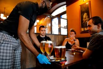 A member of bar staff wearing PPE (personal protective equipment) in the form of golves and a face mask, serves seated customers with drinks inside the Wetherspoon pub, Goldengrove in Stratford in east London on July 4, 2020, as restrictions are further eased during the novel coronavirus COVID-19 pandemic. - Pubs in England reopen on Saturday for the first time since late March, bringing cheer to drinkers and the industry but fears of public disorder and fresh coronavirus cases. (Photo by Tolga AKMEN / AFP) (Photo by TOLGA AKMEN/AFP via Getty Images)