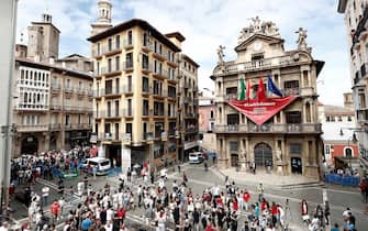 SPAIN PANDEMIC CORONAVIRUS COVID19 HOLIDAYS SANFERMINES epa08530490 People, many of them wearing the traditional white-and-red San Fermin attire, gather around noon in front of City Hall – from which hangs a giant banner in the shape of the San Fermin festival's emblematic red kerchiefs, promising 'We Will Experience Them' – in Pamplona, northern Spain, 06 July 2020. Pamplona's idiosyncratic Running of the Bulls, known as the Sanfermines, would have normally kicked off on 06 July with the 'Txupinazo' (an opening ceremony involving the firing of a pyrotechnic rocket from City Hall's main balcony). However, the bull-running festival made world-famous by Ernest Hemingway in his 1926 novel 'The Sun Also Rises' has been canceled this year due to the ongoing pandemic of the COVID-19 disease caused by the SARS-CoV-2 coronavirus. EPA/JESUS DIGES