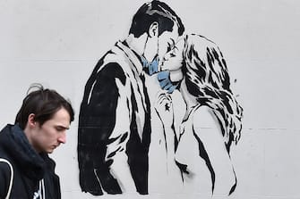 GLASGOW, SCOTLAND - MARCH 21: Members of the public walk past a new mural of a mask wearing couple kissing on March 21, 2020 in Glasgow, Scotland. Coronavirus (COVID-19) has spread to at least 182 countries, claiming over 10,000 lives and infecting more than 250,000 people. There have now been 3,269 diagnosed cases in the UK and 144 deaths.  (Photo by Jeff J Mitchell/Getty Images)