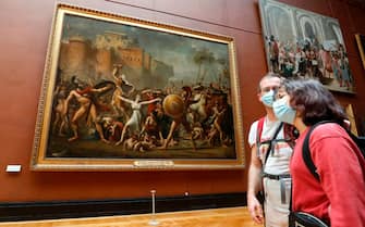 Visitors wearing face masks stand in front of  " The Intervention of the Sabine Women "  a 1799'  painting by the French painter Jacques-Louis David, at the Louvre Museum in Paris on July 6, 2020, on the museum' s reopening day. - The Louvre museum will reopen its doors on July 6, 2020, after months of closure due to lockdown measures linked to the COVID-19 pandemic, caused by the novel coronavirus. The coronavirus crisis has already caused "more than 40 million euros in losses" at the Louvre, announced its president and director Jean-Luc Martinez, who advocates a revival through "cultural democratization" and is preparing a "transformation plan" for the upcoming Olympic Games in 2024. (Photo by FRANCOIS GUILLOT / AFP) (Photo by FRANCOIS GUILLOT/AFP via Getty Images)
