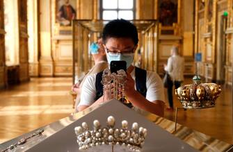 A visitor wearing face mask takes a pictures of Empress Eugenies  jewelry piece held at the Apollo gallery,  at the Louvre Museum in Paris on July 6, 2020, on the museum' s reopening day. - The Louvre museum will reopen its doors on July 6, 2020, after months of closure due to lockdown measures linked to the COVID-19 pandemic, caused by the novel coronavirus. The coronavirus crisis has already caused "more than 40 million euros in losses" at the Louvre, announced its president and director Jean-Luc Martinez, who advocates a revival through "cultural democratization" and is preparing a "transformation plan" for the upcoming Olympic Games in 2024. (Photo by FRANCOIS GUILLOT / AFP) (Photo by FRANCOIS GUILLOT/AFP via Getty Images)
