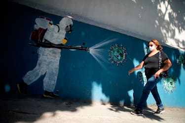 A woman walks in front of a mural depicting a man in protective suit spraying disinfectant on coronavirus with Brazilian President Jair Bolsonaro's face, at the Tijuca neighborhood in Rio de Janeiro, Brazil on July 8, 2020, amid the new coronavirus pandemic. - Brazilian President Jair Bolsonaro has tested positive for the coronavirus after months of downplaying the dangers of the disease. (Photo by MAURO PIMENTEL / AFP) (Photo by MAURO PIMENTEL/AFP via Getty Images)