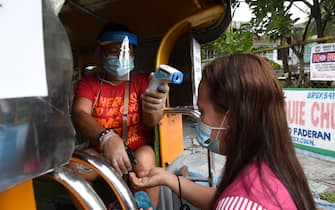 A worker (L) takes the temperature and sprays disinfectant for a passenger on a jeepney in Manila on July 6, 2020, after thousands of jeepneys hit the road again after over three months since they were forced to stop operation amid the COVID-19 coronavirus pandemic. (Photo by Ted ALJIBE / AFP) (Photo by TED ALJIBE/AFP via Getty Images)