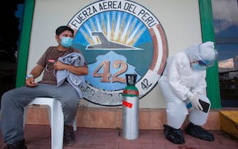 A medical worker (L) showing symptoms of the novel coronavirus COVID-19, waits for an ambulance with a relative wearing a protective suit in Iquitos, in the Amazon Forest in northern Peru, upon arriving on a plane from San Isidro community, on July 11, 2020. - Peru surpassed 320,000 cases of the novel coronavirus on July 11, while around 12,000 COVID-19 patients remain hospitalized and more than 11,600 have died. Peru, with 33 million inhabitants, is the second country in Latin America with the most cases of COVID-19, behind Brazil, and stands fifth in the world. (Photo by Cesar Von BANCELS / AFP) (Photo by CESAR VON BANCELS/AFP via Getty Images)