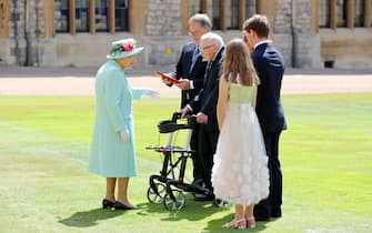 Britain's Queen Elizabeth II (L) talks to 100-year-old veteran Captain Tom Moore and his family during an investiture to confer the honour of knighthood upon him at Windsor Castle in Windsor, west of London on July 17, 2020. - British World War II veteran Captain Tom Moore was made a a Knight Bachelor (Knighthood) for raising over £32 million for the NHS during the coronavirus pandemic. (Photo by Chris Jackson / POOL / AFP) (Photo by CHRIS JACKSON/POOL/AFP via Getty Images)