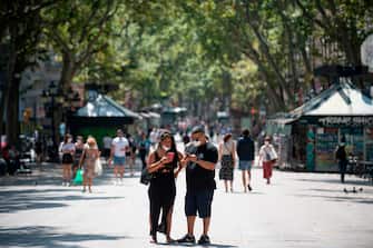 People wearing face masks look at their phones at Las Ramblas street in Barcelona on July 18, 2020. - Four million residents of Barcelona have been urged to stay at home as virus cases rise, while EU leaders were set to meet again in Brussels, seeking to rescue Europe's economy from the ravages of the pandemic. (Photo by Josep LAGO / AFP) (Photo by JOSEP LAGO/AFP via Getty Images)