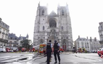 French Police officers stand ready as firefighters are at work to put out a fire at the Saint-Pierre-et-Saint-Paul cathedral in Nantes, western France, on July 18, 2020. - A blaze that broke inside the gothic cathedral of Nantes on July 18 has been contained, emergency officials said, adding that the damage was not comparable to last year's fire at Notre-Dame cathedral in Paris. "The damage is concentrated on the organ, which seems to be completely destroyed. Its platform is very unstable and could collapse," regional fire chief General Laurent Ferlay told a press briefing in front of the cathedral. (Photo by Sebastien SALOM-GOMIS / AFP) (Photo by SEBASTIEN SALOM-GOMIS/AFP via Getty Images)