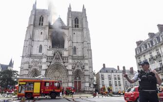 A French Police officer gestures as firefighters are at work to put out a fire at the Saint-Pierre-et-Saint-Paul cathedral in Nantes, western France, on July 18, 2020. - The major fire that broke out on July 18, 2020 inside the cathedral in the western French city of Nantes has now been contained, emergency services said. "It is a major fire," the emergency operations centre said, adding that crews were alerted just before 08:00 am (0600 GMT) and that 60 firefighters had been dispatched. (Photo by Sebastien SALOM-GOMIS / AFP) (Photo by SEBASTIEN SALOM-GOMIS/AFP via Getty Images)