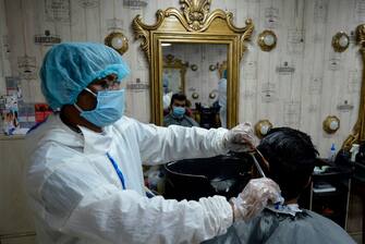 A barber wearing protective cloths gives a haircut to a client at a barber shop amid concerns over the spread of the COVID-19 coronavirus, in Dhaka on July 7, 2020. (Photo by MUNIR UZ ZAMAN / AFP) (Photo by MUNIR UZ ZAMAN/AFP via Getty Images)
