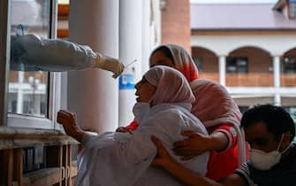 Relatives hold an elderly woman (C) as a health worker takes a nasal swab sample to test for the COVID-19 coronavirus at a testing centre in Srinagar on July 21, 2020. - India on July 17 hit a million coronavirus cases, the third-highest total in the world, with no sign yet of the infection curve flattening as new cases emerge in rural areas. More than 25,000 people have died nationally. (Photo by TAUSEEF MUSTAFA / AFP) (Photo by TAUSEEF MUSTAFA/AFP via Getty Images)