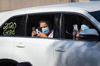 epa08557583 Family members of a graduate take pictures while wearing masks at a graduation ceremony at the California High School amid the coronavirus pandemic in Whittier, California, USA, 20 July 2020. Friends and family members were required to stay in their cars as the students were handed their diplomas by school staff who were social distancing and wearing masks, due to the coronavirus pandemic.  EPA/CHRISTIAN MONTERROSA