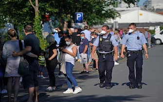 GUETERSLOH, GERMANY - JUNE 24: Police walk past a line of people waiting to be tested for Covid-19 infection following a Covid-19 outbreak at the nearby Toennies meat packaging center on June 24, 2020 in Guetersloh, Germany. The line at the Carl Miele vocational school, which is being used a Covid testing site, stretched approximately one kilometer long. Many of those waiting are hoping to go on vacation abroad soon and are concerned they will need certification of being free of infection. Over 1,500 employees of the plant have been confirmed to be infected and authorities are racing to stem a further spread of the virus. The Bundeswehr, the German armed forces, has stepped in to help test people at the approximately 250 houses and apartment buildings where Toennies employees, many of whom come from Romania, Bulgaria and Poland, live throughout the Guetersloh region. (Photo by Sean Gallup/Getty Images)