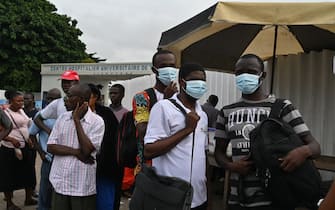 TOPSHOT - People wear protective masks as they wait at a bus stop outside Treichville university hospital, on March 11, 2020, where the first Ivorian case of new coronavirus was confirmed.  The Ivorian case is a 45-year-old man who had recently stayed in Italy, the government said on March 11, 2020. (Photo by ISSOUF SANOGO / AFP) (Photo by ISSOUF SANOGO/AFP via Getty Images)