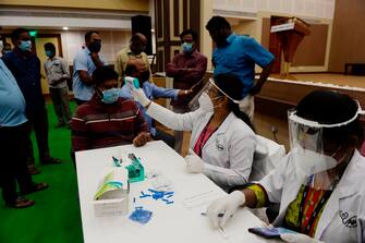 A medical technician (C) takes the body temperature of a man before taking a sample for a COVID-19 anti-body tests at a temporary testing facility for frontline workers during a lockdown as a preventive measure against the COVID-19 coronavirus in Chennai on July 16, 2020. (Photo by Arun SANKAR / AFP) (Photo by ARUN SANKAR/AFP via Getty Images)