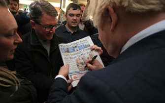 1188625897 COUNTY DURHAM, ENGLAND - DECEMBER 14: UK Prime Minister Boris Johnson signs a copy of The Northern Echo for a supporter on a visit to meet newly elected Conservative party MP for Sedgefield, Paul Howell at Sedgefield Cricket Club on December 14, 2019 in County Durham, England. Following his Conservative party's general election victory, Prime Minister Boris Johnson called on Britons to put years of bitter divisions over the country's EU membership behind them as he vowed to use his resounding election victory to finally deliver Brexit next month. (Photo by Lindsey Parnaby - WPA Pool/Getty Images)