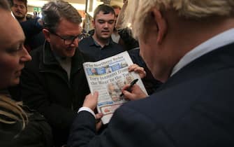 COUNTY DURHAM, ENGLAND - DECEMBER 14: UK Prime Minister Boris Johnson signs a copy of The Northern Echo for a supporter on a visit to meet newly elected Conservative party MP for Sedgefield, Paul Howell at Sedgefield Cricket Club on December 14, 2019 in County Durham, England. Following his Conservative party's general election victory, Prime Minister Boris Johnson called on Britons to put years of bitter divisions over the country's EU membership behind them as he vowed to use his resounding election victory to finally deliver Brexit next month. (Photo by Lindsey Parnaby - WPA Pool/Getty Images)