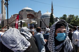 1257921160 ISTANBUL, TURKEY - JULY 24: People gather before the first official Friday prayers outside Hagia Sophia Mosque on July 24, 2020 in Istanbul, Turkey. Turkey's President Recep Tayyip Erdogan attended the first Friday prayer inside the Hagia Sophia Mosque after it was officially reconverted into a mosque from a museum. The controversial decision to change the iconic buildings status came after Turkey's highest administrative court voted on July, 10 to revoke the structures status as a museum allowing it to be converted back to a mosque. Throughout it's history the UNESCO World Heritage site has served as a Byzantine Cathedral, a mosque under Ottoman rule, and most recently a museum. Thousands of worshippers from all over Turkey flocked to the site for the chance to pray inside the historic building for the first Friday prayers. (Photo by Burak Kara/Getty Images)