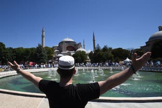 A man raises his arms as people gathe on July 24, 2020 outside Hagia Sophia in Istanbul to attend the Friday prayer, the first muslim prayer held at the landmark since it was reconverted to a mosque despite international condemnation. - A top Turkish court revoked the sixth-century monument's status as a museum on July 10 and Turkish President then ordered the building to reopen for Muslim worship. The UNESCO World Heritage site in historic Istanbul was first built as a cathedral in the Christian Byzantine Empire but was converted into a mosque after the Ottoman conquest of Constantinople in 1453. (Photo by OZAN KOSE / AFP) (Photo by OZAN KOSE/AFP via Getty Images)