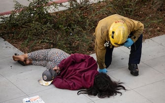 epa08566521 A fire fighter checks on a protestor named sRoxanne who lay on the pavement after she was arrested during clashes between police and protesters in front the Federal Court House during a Black Lives Matter and Anti Fascist protest in Los Angeles, California, USA, 25 July 2020. Hundreds of Black Lives Matter protested against racism and police brutality and in support of the Portland's demonstrations.  EPA/ETIENNE LAURENT