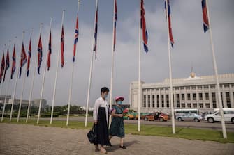 Two women wearing face masks walk past a row of North Korean flags to pay their respects on the occasion of 26th anniversary of Kim Il Sung's death, at Mansu hill in Pyongyang on July 8, 2020. (Photo by KIM Won Jin / AFP) (Photo by KIM WON JIN/AFP via Getty Images)