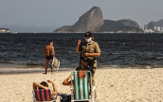 1227793316 NITEROI, BRAZIL - JULY 26: A police officer asks beach goers to leave at Icarai Beach amidst the coronavirus (COVID-19) pandemic on July 26, 2020 in Niteroi, Brazil. The practice of physical activities on boardwalks and individual sports at sea is allowed. However, the use of chairs and tents on the sand is still prohibited. Starting next week group sports such as volleyball and football can be practiced, but only on weekdays. (Photo by Luis Alvarenga/Getty Images)
