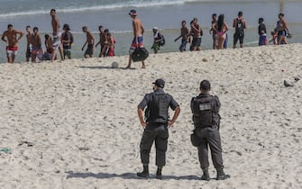 RIO DE JANEIRO, BRAZIL - JULY 26: Police officers observe a group of young people leaving Arpoador Beach amidst the coronavirus (COVID-19) pandemic on July 26, 2020 in Rio de Janeiro, Brazil. The practice of physical activities on boardwalks and individual sports at sea is allowed. However, the use of chairs and tents on the sand is still prohibited. Starting next week group sports such as volleyball and football can be practiced, but only on weekdays. (Photo by Andre Coelho/Getty Images)