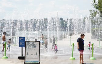 NEW YORK, NEW YORK - AUGUST 01: A sign reads "Protect yourself and others, wear a mask to stop the spread of Covid-19" as people play at a park sprinkler during Phase 4 of re-opening following restrictions imposed to curb the coronavirus pandemic on August 1, 2020 in New York, New York. The fourth phase allows outdoor arts and entertainment, sporting events without fans and media production. (Photo by Rob Kim/Getty Images)