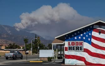 CHERRY VALLEY, CA - AUGUST 02: Smoke from the Apple Fire is seen behind a stars and stripes painted building in the community of Calimesa on August 2, 2020 near Cherry Valley, California. The wildfire has spread across more than 20,000 acres and forced 7,000 residents from their homes.  (Photo by David McNew/Getty Images)