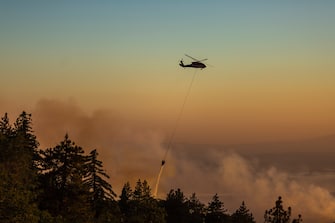 CHERRY VALLEY, CA - AUGUST 01: A helicopter drops water on the Apple Fire as an excessive heat warning continues on August 1, 2020 in Cherry Valley, California. The fire began shortly before 5 p.m. the previous evening, threatening a large number of homes overnight and forcing thousands to flee before exploding to 12,000 acres this afternoon, mostly climbing the steep wilderness slopes of the San Bernardino Mountains.  (Photo by David McNew/Getty Images)