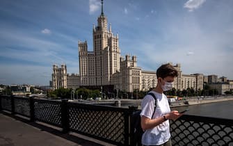 A woman wearing a face mask to protect against the coronavirus disease walks on a bridge in front of a Stalin-era skyscraper in central Moscow on August 5, 2020. (Photo by Yuri KADOBNOV / AFP) (Photo by YURI KADOBNOV/AFP via Getty Images)