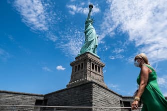 NEW YORK, NY - JULY 20: A visitor wearing a protective mask walks past the Statue of Liberty as it reopened on Liberty Island on July 20, 2020 in New York City. Liberty Island is partially reopening months after the attraction was shut down due to the coronavirus pandemic. Access to Liberty Island has reopened but the statue itself, the pedestal and museum remain closed. (Photo by Jeenah Moon/Getty Images)