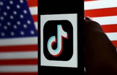 In this photo illustration, the social media application logo, TikTok is displayed on the screen of an iPhone on an American flag background on August 3, 2020 in Arlington, Virginia. - President Donald Trump said Monday that Chinese-owned hugely popular video-sharing app TikTok will be "out of business" in the United States if not sold to a US firm by September 15, 2020."I set a date of around September 15, at which point it's going to be out of business in the United States," he told reporters. (Photo by Olivier DOULIERY / AFP) (Photo by OLIVIER DOULIERY/AFP via Getty Images)