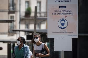 People wear protective face masks as they stroll along a street next to a sign reading "Here the mask is mandatory" in Nantes, western France on August 21, 2020, as face masks became compulsory in the city center and some areas to stem the spread of the COVID-19 disease caused by the novel coronavirus. (Photo by Loic VENANCE / AFP) (Photo by LOIC VENANCE/AFP via Getty Images)