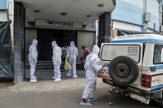 Health workers wearing Personal Protective Equipment (PPE) suits guide asymptomatic COVID-19 patients from an ambulance (R) to the entrance of the Siliguri Indoor Stadium, temporarily converted into a COVID-19 coronavirus safe home care centre, in Siliguri on August 21, 2020. (Photo by DIPTENDU DUTTA / AFP) (Photo by DIPTENDU DUTTA/AFP via Getty Images)