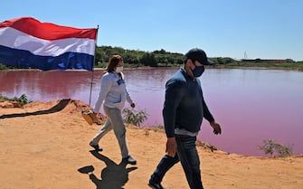 Locals gather at the shore of the Cerro Lake, formed from a meander of the Paraguay River, to protest against a nearby tannery (background) which allegedly throws chemical disposals into the lake causing its water to turn pinkish red, in Limpio, 25 km northeast of Asuncion, on August 22, 2020. - According to experts from the National University Multidisciplinary Lab, the colour of the water is due to the presence of heavy metals like iron, chromium, and zinc, among others, commonly used in the tanning process. (Photo by Norberto DUARTE / AFP) (Photo by NORBERTO DUARTE/AFP via Getty Images)