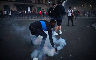 PARIS, FRANCE - AUGUST 23: A Paris Saint Germain fan picks up a tear gas round during violent confrontations with police outside PSG's Parc de Princes Stadium as the Champions League Final was being played on August 23, 2020 in Paris, France. Paris Saint German football team have reached the 2019/20 UEFA Champions League finals for the first time in their history, just eleven days after celebrating their 50th Anniversary, taking on five-time winners Bayern Munich at the Estádio da Luz in Lisbon. (Photo by Kiran Ridley/Getty Images)