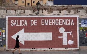 A woman wearing a face mask walks past a mural reading "Emergency exit" in Malaga on August 23, 2020. - Despite having imposed draconian coronavirus lockdown and making the use of face masks in public mandatory, Spain is once again a world hotspot for the COVID-19 pandemic. The country has nearly 378,000 confirmed cases of the respiratory disease, the highest amount in Western Europe, and one of the fastest growth rates on the continent. (Photo by JORGE GUERRERO / AFP) (Photo by JORGE GUERRERO/AFP via Getty Images)