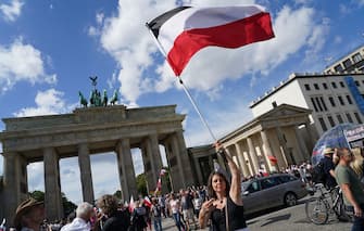 BERLIN, GERMANY - AUGUST 29: A woman waves a German Empire flag and displays a hand signal in support of vegan chef and conspiracy theories proponent Attila Hildmann at the Brandenburg Gate during protests against coronavirus-related restrictions and government policy on August 29, 2020 in Berlin, Germany. Tens of thousands of people from a wide spectrum, including coronavirus skeptics, conspiracy enthusiasts, hippies, right-wing extremists, religious conservatives and others converged on Berlin to attend the protests. City authorities had banned the protests, citing the flouting of social distancing by participants in a similar march that drew at least 17,000 people a few weeks ago, but a court overturned the ban. (Photo by Sean Gallup/Getty Images)