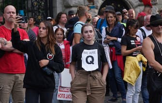 BERLIN, GERMANY - AUGUST 29: Mostly right-wing protesters, including a young woman wearing a QAnon shirt, observe riot police clearing Unter den Linden avenue during protests against coronavirus-related restrictions and government policy on August 29, 2020 in Berlin, Germany. Tens of thousands of people from a wide spectrum, including coronavirus skeptics, conspiracy enthusiasts, hippies, right-wing extremists, religious conservatives and others converged on Berlin to attend the protests. City authorities had banned the protests, citing the flouting of social distancing by participants in a similar march that drew at least 17,000 people a few weeks ago, but a court overturned the ban. (Photo by Sean Gallup/Getty Images)