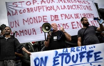 A man shouts in a megaphone in front of a banner reading "Stop lies, to corruption, to dictatorship, A world of peace, of freedom, of love for our children, during a protest against the mandatory wearing of face masks on the Place de La Nation in Paris on August 29, 2020, amid the Covid-19 (novel coronavirus) pandemic. - Masks, which were already compulsory on public transport, in enclosed public spaces, and outdoors in Paris in certain high-congestion areas around tourist sites, were made mandatory outdoors citywide on August 28 to fight the rising coronavirus infections. (Photo by Christophe ARCHAMBAULT / AFP) (Photo by CHRISTOPHE ARCHAMBAULT/AFP via Getty Images)