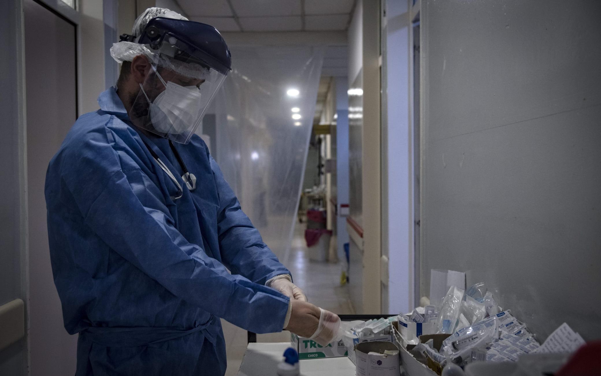 1228411434 Dr Mario Grossmann wearing protective suit puts on gloves before treating patients with COVID-19, during his 24hs shift, at the emergency area of the Doctor Alberto Antranik Eurnekian Public Hospital in Ezeiza, in the outskirts of Buenos Aires on August 29, 2020, amid the new coronavirus, COVID-19, pandemic. - Dr Grossmann, a professor, head of practical work of semiology and internal medicine at Buenos Aires University (UBA) and chair head of semiology and internal medicine at Universidad Abierta Interamericana (UAI) teaches from the hospital through video calls to students of 4th and 5th year. (Photo by ARIEL TIMY TORRES / AFP) (Photo by ARIEL TIMY TORRES/AFP via Getty Images)